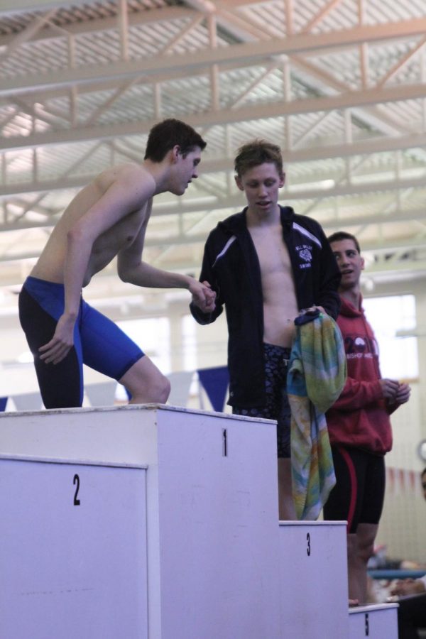After receiving his fifth-place medal in the 200 individual medley, junior Chris Sprenger helps the third pace swimmer onto the podium on Saturday, Feb. 17.