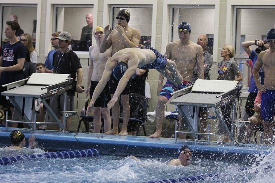 Junior Chris Sprenger dives off the block as junior Ethan Forristal reaches the wall during the 200 freestyle relay preliminary round on Friday, Feb. 16.