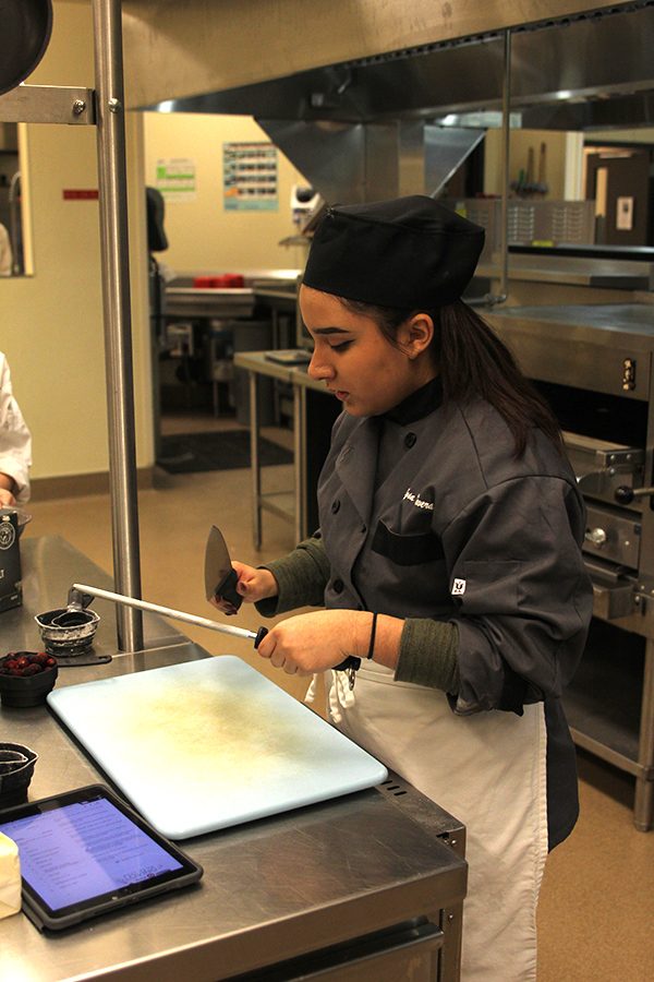 While holding a knife, senior Alyssa Talavera uses a sharpening rod to sharpen the knife.