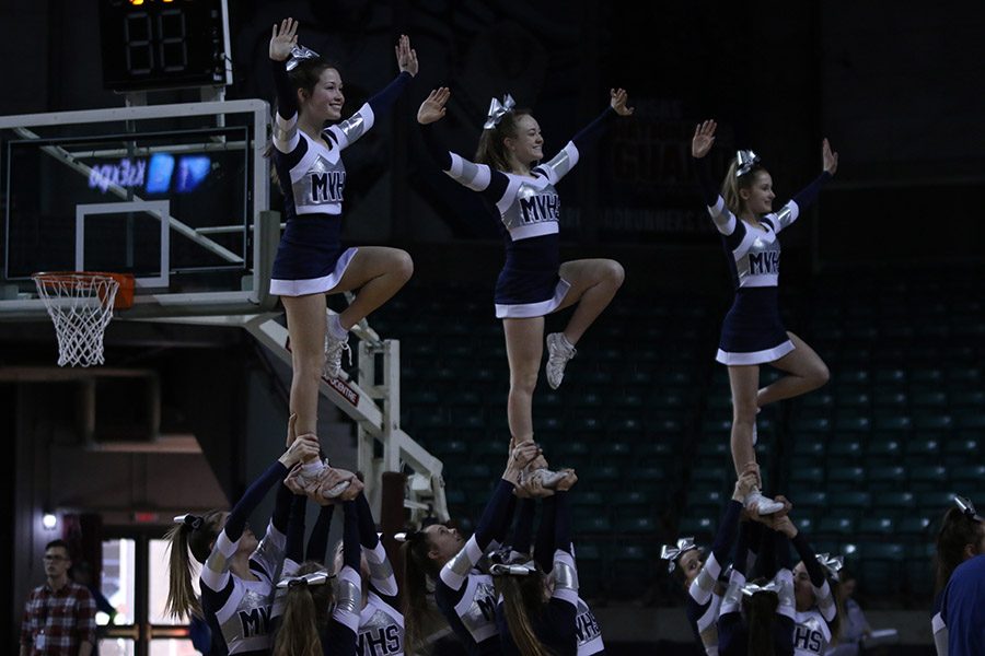 While hitting a stunt, cheerleaders cheer on the girls.