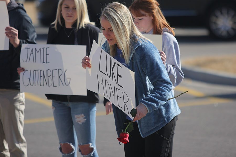 Holding a sign to remember Parkland victim Luke Hoyer, senior Adde Hinkle bends to drop a rose.