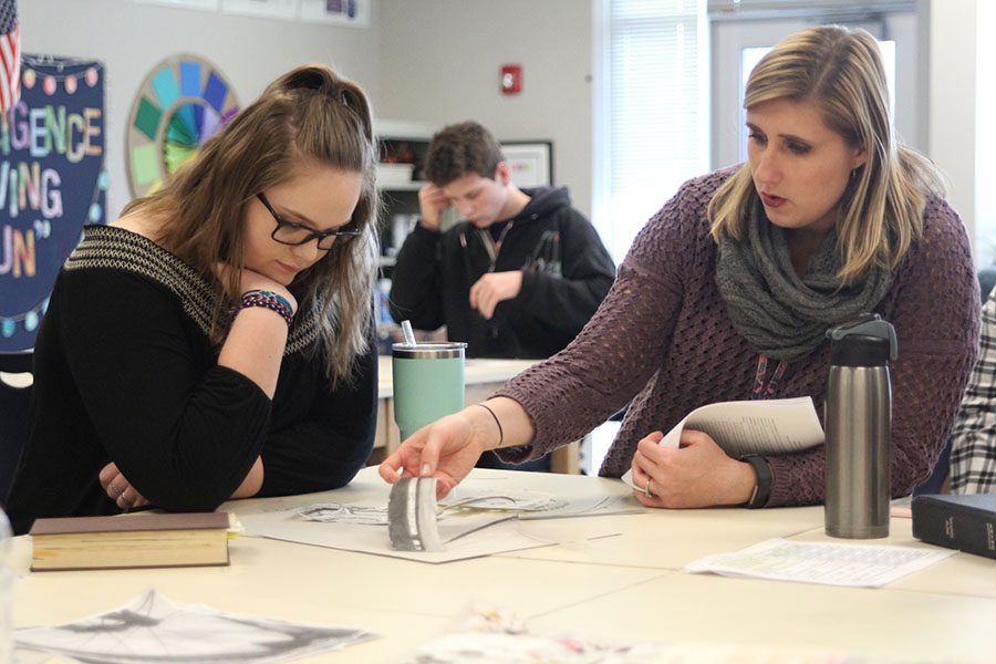 Rearranging strips of paper in order to create a better pattern, art teacher Krystal Strong helps senior Mikala Postlewait construct her negative space project during drawing class on Tuesday, April 10. “I chose to draw a bike for my project. We created three drawings and used three different mediums for each one. After finishing the drawings, I cut away the negative space and created a different background,” Postlewait said. “I enjoyed being able to choose what I wanted to draw and being able to use different mediums for each drawing because I got to use things that I hadn’t experimented with before, like charcoal.” 