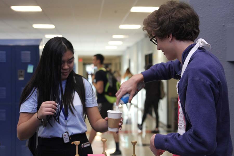 In the main foyer before class on  Friday, April 13, senior Brady Watkins works for the Catty Shack and squirts whipped cream on junior Ally Nguyen's coffee. "I like using the whipped cream to express my emotional, artistic abilities," Watkins said.