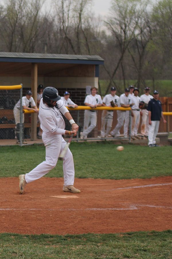 As his team cheers him on, junior Ethan Keopke hits the ball into the outfield.