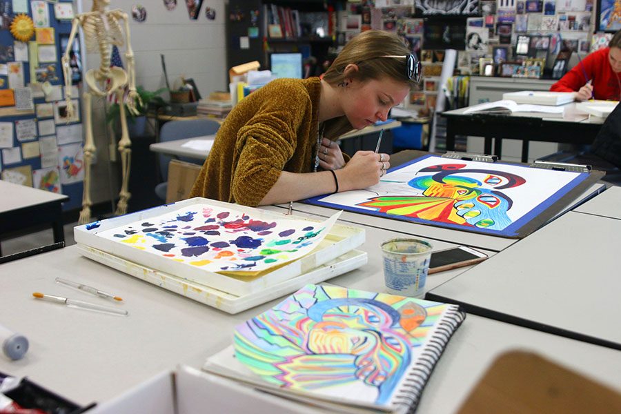 Surrounded by her color pencil sketch, paint brushes and swatches of paint, senior Mary Kate Stoneburner focuses on detailing the outer edge of her painting on Tuesday, April 10. With the intent to add bright colors to her cultural unity painting, Stoneburner incorporates symbols from different religions and cultures. “This is my fourth time taking Advanced Painting and I love it,” Stoneburner said. “We make a lot of different projects that use a lot of different supplies that allow people’s interests and talents to be showcased.”