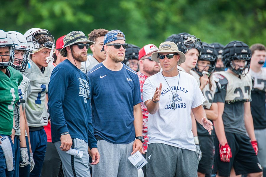 With players standing behind them, football coaches Kody Cook, Zack McFall and head coach Joel Applebee watch the football team as they participate at the Blue Springs South football camp on Thursday, June 7.