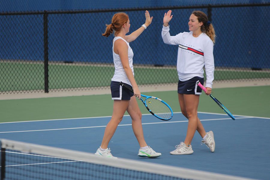 Celebrating a good shot, doubles partners Josie Carey and Sydney Fisher high five while trading positions on the court.