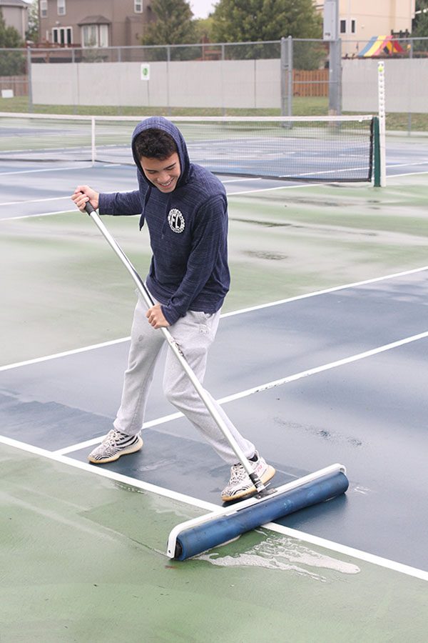 Smiling, senior Eric Schanker cleans the courts with the sponge roller. Despite the effort, rain fell again and the regional tournament was delayed for four more hours.