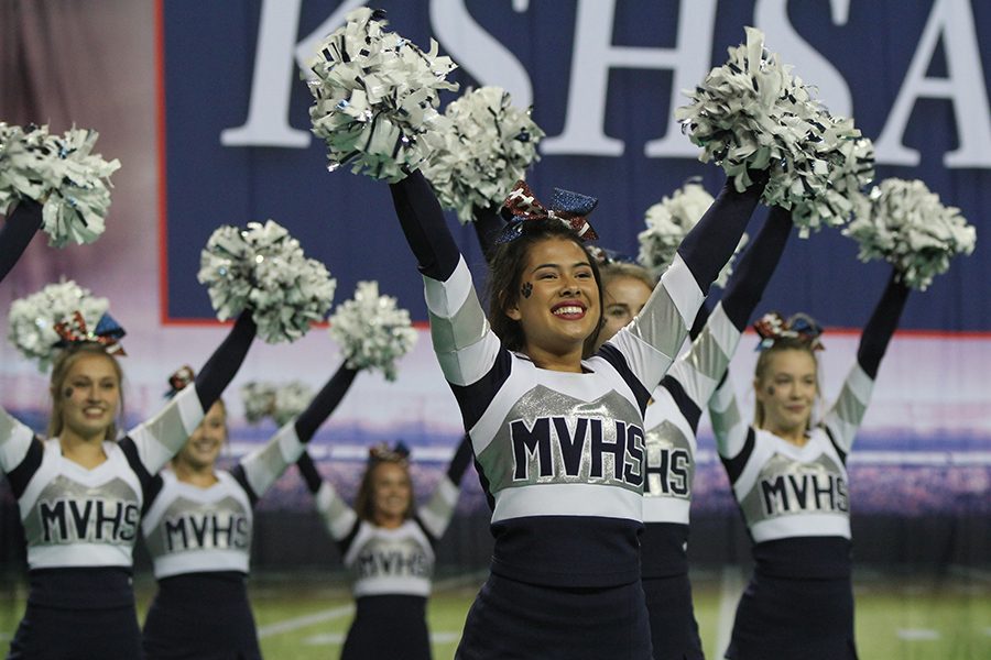 Facing the audience, senior Mya Johnston poses with her poms in the air. I am very proud of my team as a whole, Johnston said. 6A was full of hard competition and really good teams, but we competed to the best of our ability and definitely left it all out on the mat.