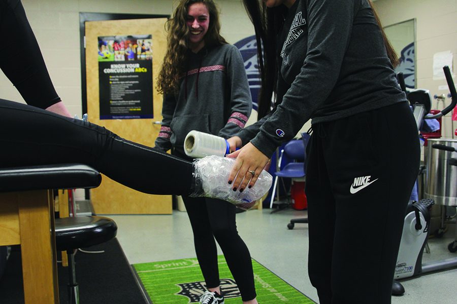 Student+trainers+junior+Maddie+Valencia+and+sophomore+Katie+Turner+wrap+blank+Claire+Kaifes+foot+in+ice+on+Tuesday%2C+Jan.+22%2C+%E2%80%9CWe+see+a+lot+of+tendonitis%2C+concussions%2C+ankle+sprains%E2%80%9D+said+Valencia.