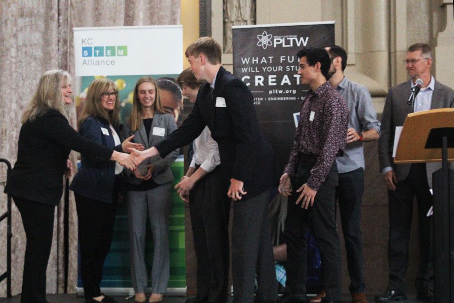 Seniors Aniston Cumbie, Andrew Thomas, Harry Ahrenholtz and Matthew Richle shake the hands of prominent engineers and KC Stem Alliance organizers as they receive recognition for their innovation award.