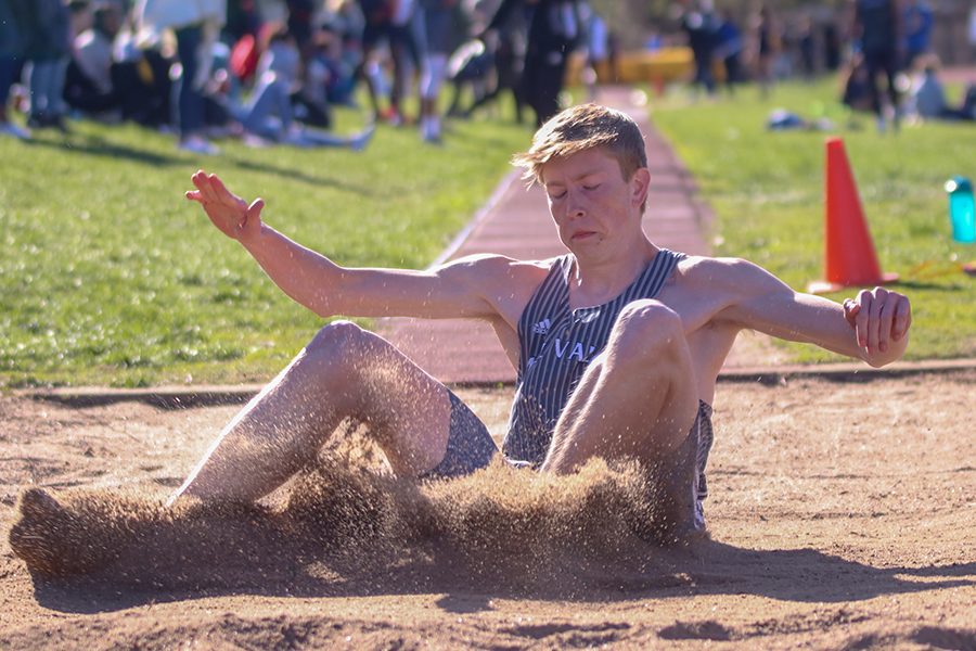 After running down the runway in the long jump, senior Harry Ahrenholtz lands in the sand pit.