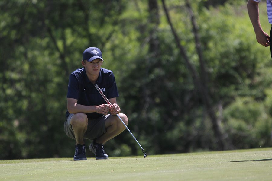 Kneeling on the green at hole 8, senior Blake Aerni waits patiently for his competitors to putt.