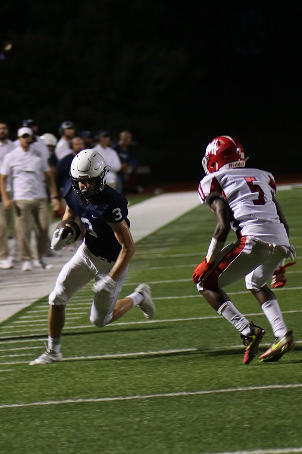 In possession of the ball, junior Jacob Hartman runs past Miege defense.