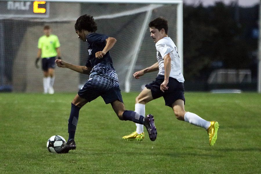 Trying to catch up to the ball, junior Cael Denney runs alongside his opponent.