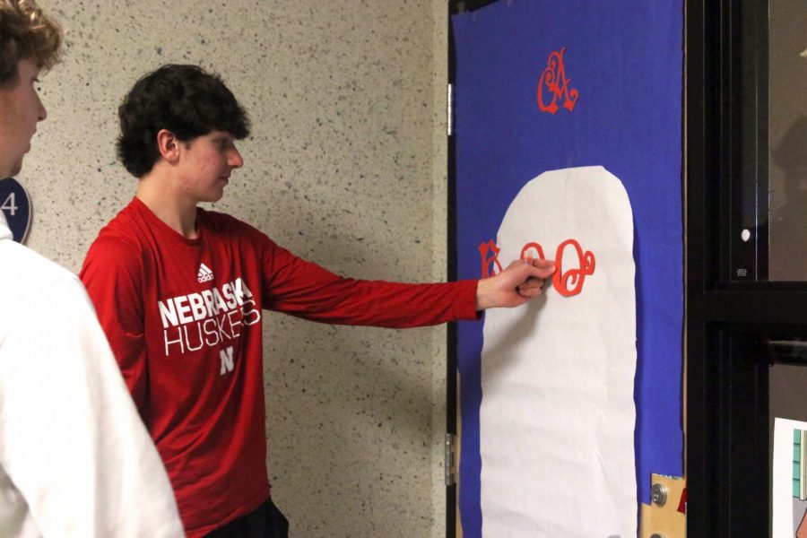 Holding up a letter, junior Caden Gurwell decorates his seminar’s door.