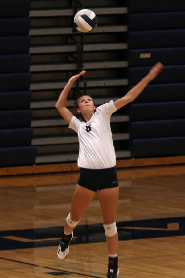 About to serve the ball, sophomore Amara Traiger extends her arm above her head.