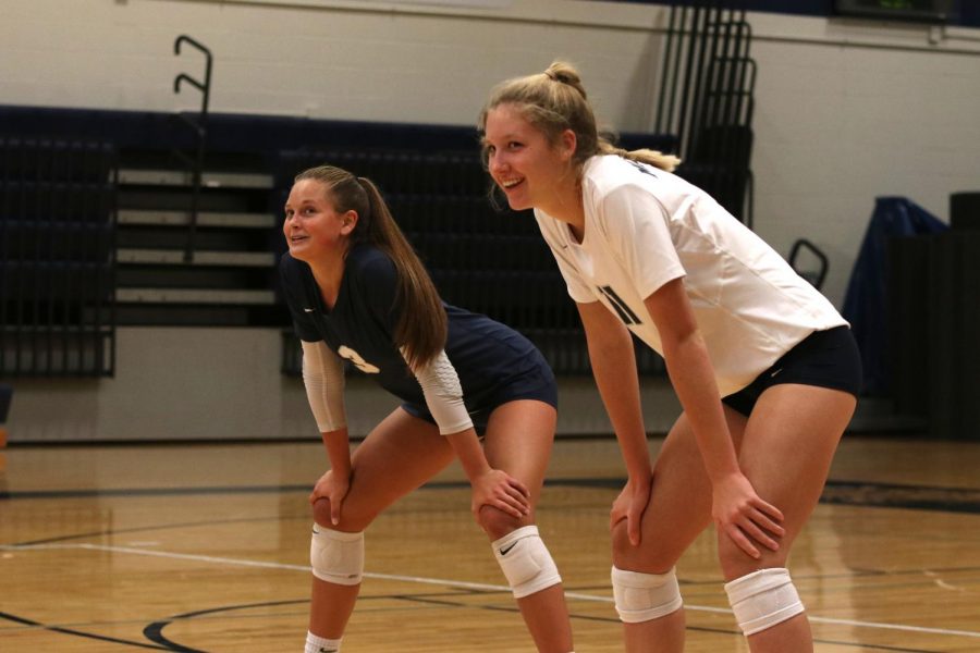 Awaiting the serve from the other team, sophomore Kate Roth and junior Jaden Ravnsborg smile at their fellow teammates on Thursday, Oct. 3.