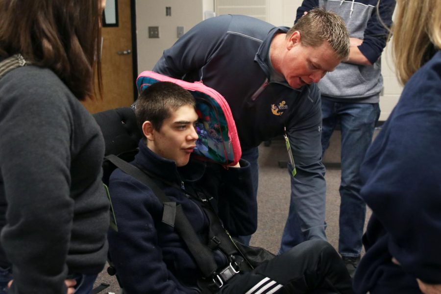 Dave Hayden explains the placement of Olathe West senior Ty Hayden’s harness to the four Engineering Design and Development students on Friday, Nov.15. For their year-long project, they hope to create a modified seat belt that will help with transportation for people with special needs.