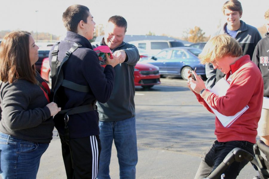 Holding up his phone, senior Alex Heinking takes pictures of Olathe West senior Ty Hayden wearing the harness.