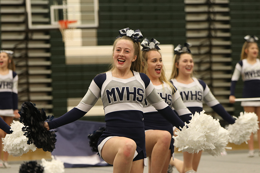 Kneeling to the ground, junior Emma Moore puts on a smile while shaking her pom-poms.