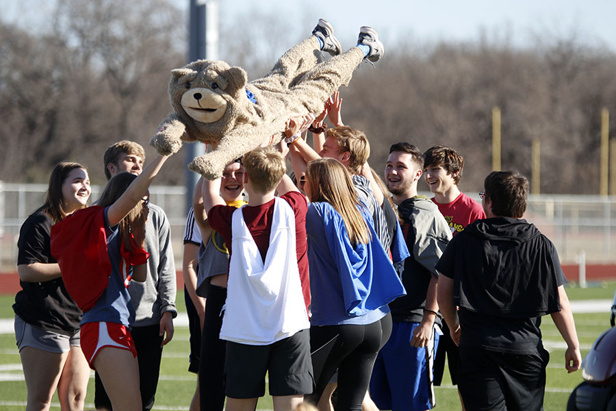 Wearing a bear costume, freshman Eli Olsen is held up by his teammates.