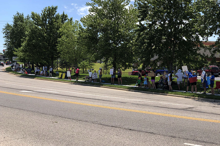 Holding signs and shouting chants, families gather on the sidewalk along Hilltop Drive to share a message to drivers.
