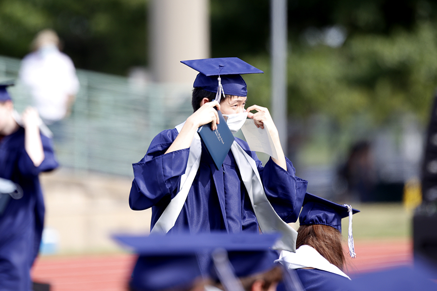 After getting his picture taken, senior Kevin Lee puts his mask back on his face as he makes his way back to his seat. 
