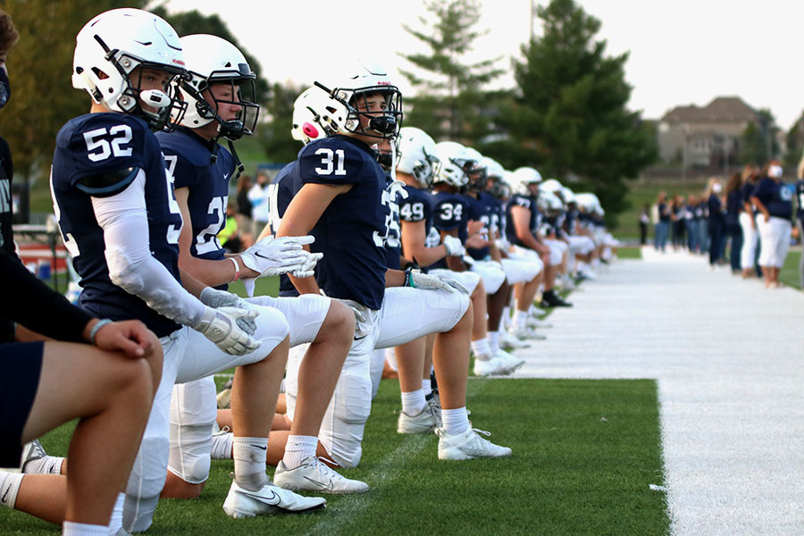 On the sideline, defensive back Mark Bauer gets on one knee to recognize the seniors being acknowledged on senior night. 