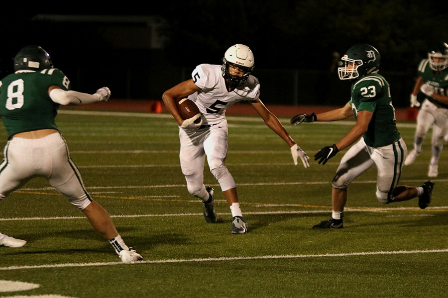 Running between two De Soto opponents, wide receiver Kendrick Jones sprints with the ball. 