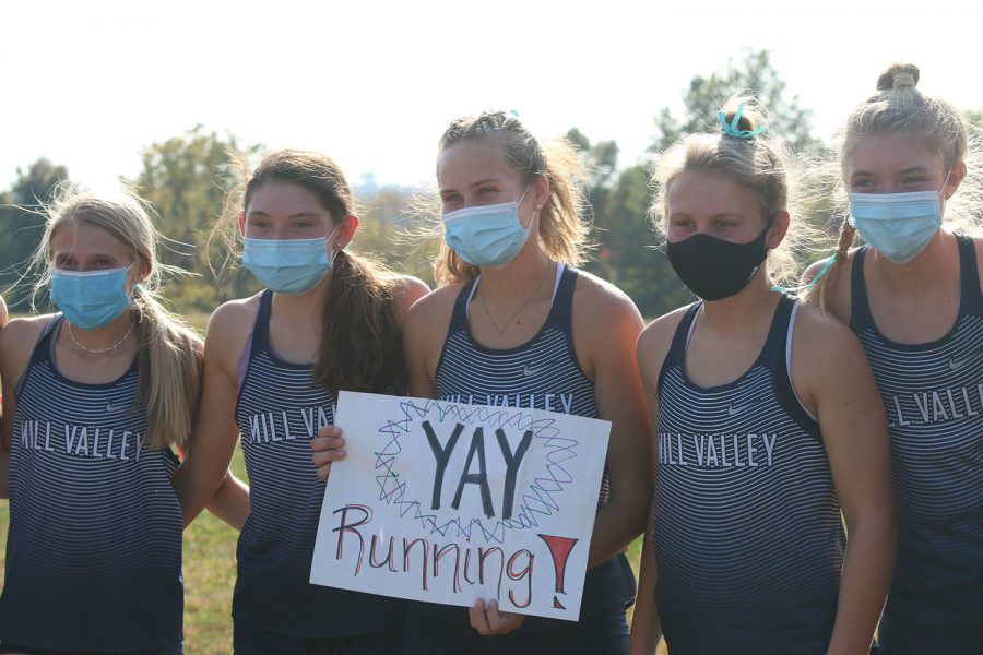 Posing for a picture, a few varsity cross country girls take a picture with a sign before they run.