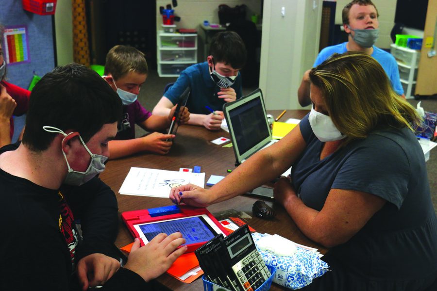 While gathered around the table, special education teacher Sara Evans helps junior Gabe Fuller complete an activity on an iPad during her daily living class Monday, Sept. 28.