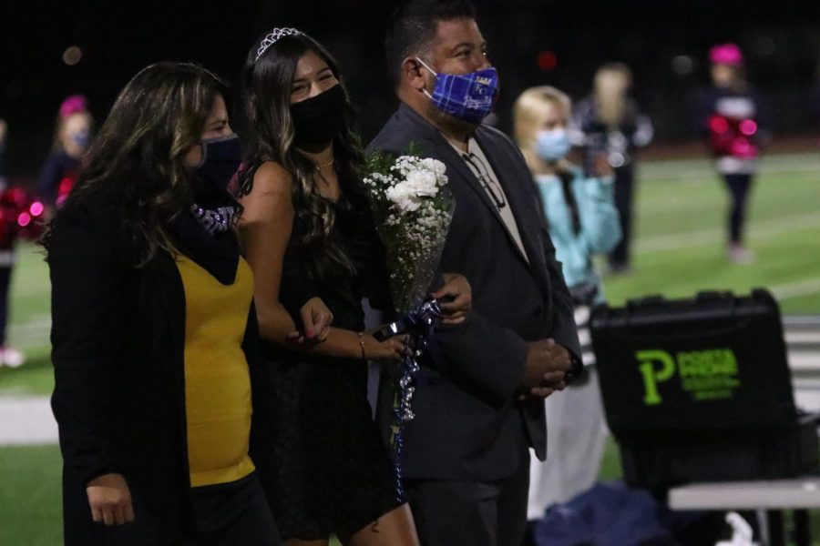 As she walks with her arms interlocked with her parents, senior Isabella Loya smiles while walking to meet up with her partner.