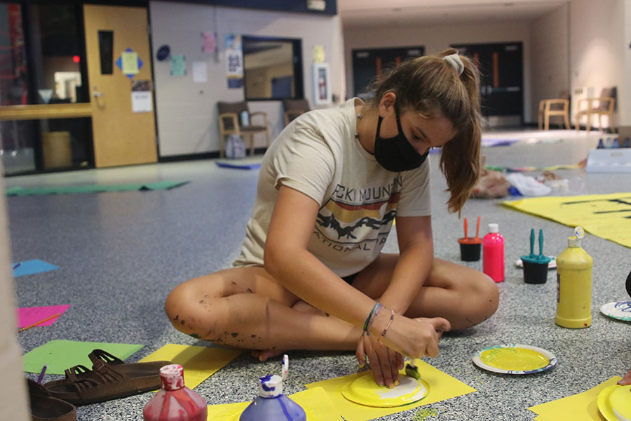 Sitting on the floor, freshmen Lauren Prestia paints a plate yellow. StuCo and volunteer students got together to decorate the school in class colors for Homecoming week on Sunday Oct. 11. 
