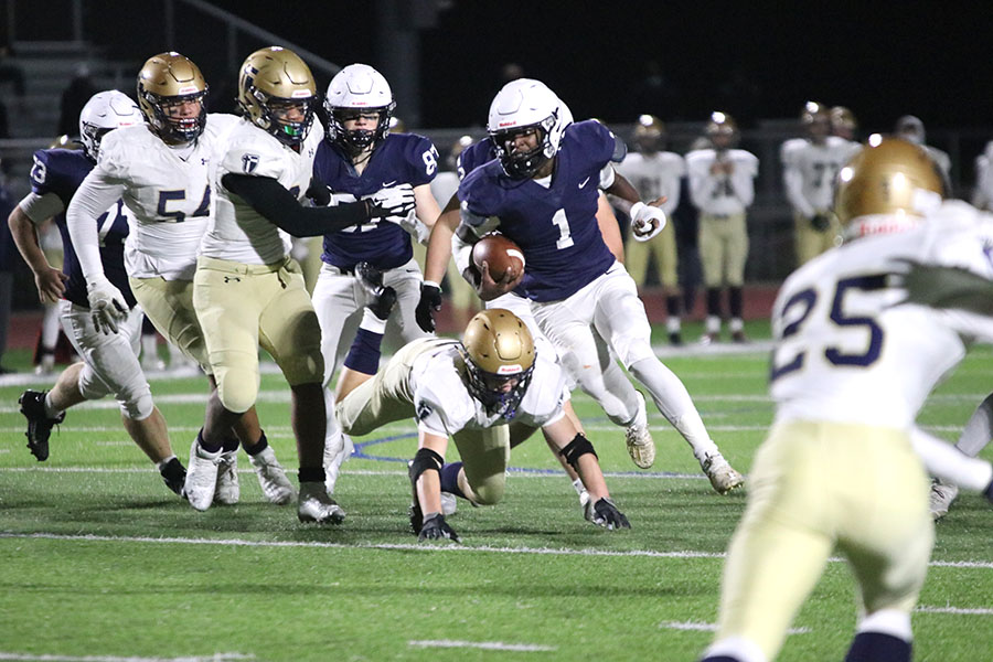 To dodge being tackled, running back Quin Wittenauer carries the ball between an opening in the middle of the field to run the ball towards the end zone. 