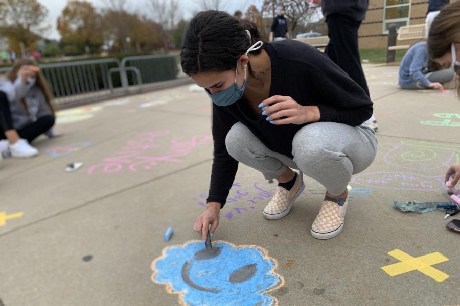 Bent+down+with+a+piece+of+black+chalk+in+her+hands%2C+senior+Nicole+Crist+draws+a+happy+cloud+at+Prairie+Ridge+Elementary%2C+Wednesday%2C+Nov.+4%2C+to+bring+positivity+to+the+elementary+students+for+the+end+of+the+quarter+with+several+other+members+of+the+National+Honor+Society.+