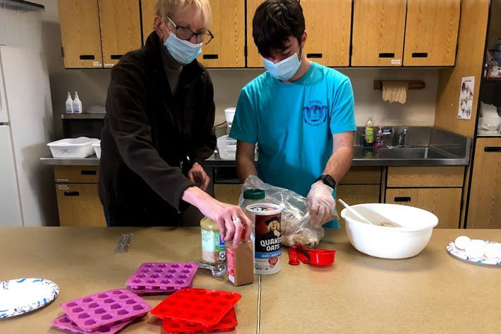 Scooping out a cup of quick oats, Bridge student Nick Pettigrew is assisted by a para as he prepares the dog treat mix Friday, Dec. 4.