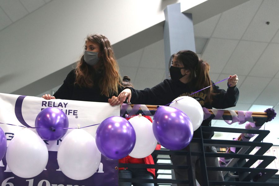 Hanging up the balloons, junior Deema Rashid and senior Addison Stover tape the balloons onto the railing.