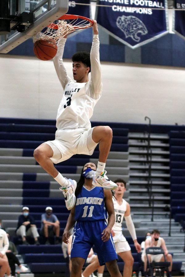 Holding onto the rim of the basket, junior Adrian Dimond dunks the ball in the last few minutes of the fourth quarter to finish the game strong. 