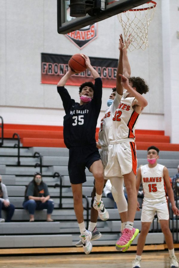 Jumping up in the air, junior Adrian Dimond reaches towards the basket with the ball in his hands. 