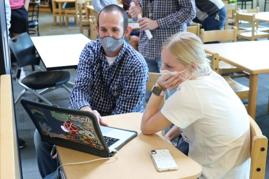 Looking at a school-issued MacBook, Director of Technology Brandon Riffle and junior Abby Steiger work to open up storage space for the macOS Big Sur update Friday, April 2.