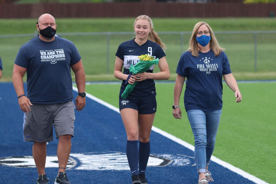 Walking with her parents, senior girls soccer player Mia Colletti holds a bouquet of flowers as she approaches the middle of the field. 