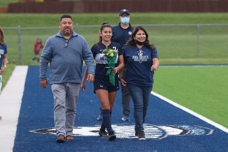 Walking with her parents, senior girls soccer player Isabella Loya holds a bouquet of flowers as she approaches the middle of the field. 