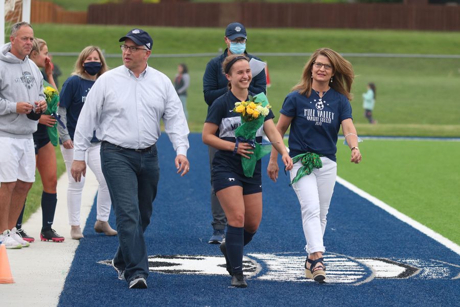 Walking with her parents, senior girls soccer player Avery Norman holds a bouquet of flowers as she approaches the middle of the field. 