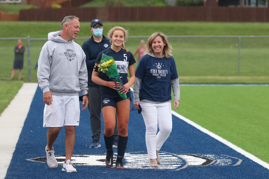 Walking with her parents, senior girls soccer player Molly Ricker holds a bouquet of flowers as she approaches the middle of the field. 