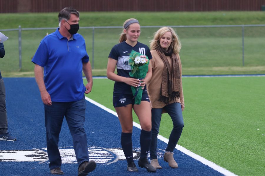 Walking with her parents, senior girls soccer player Emma Schieber holds a bouquet of flowers as she approaches the middle of the field. 