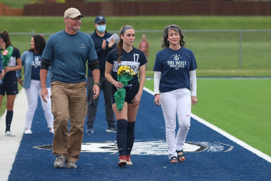 Walking with her parents, senior girls soccer player Katie Turner holds a bouquet of flowers as she approaches the middle of the field. 