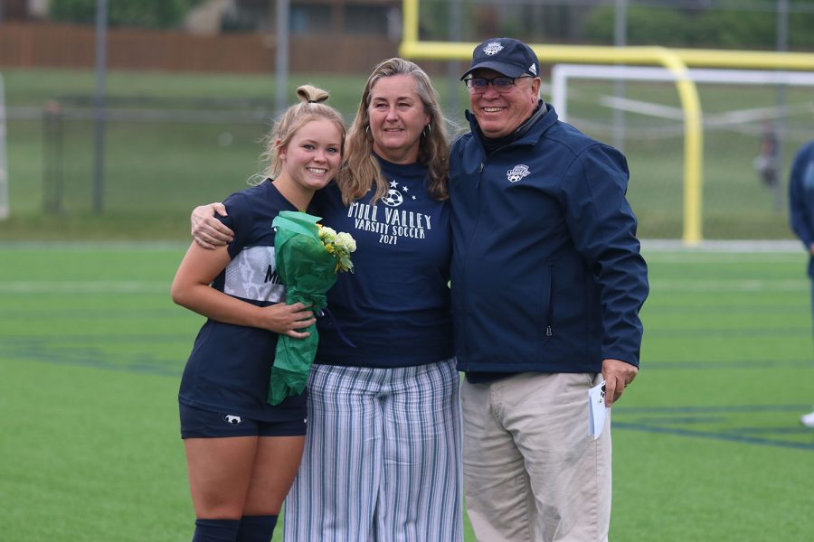 Posing with her parents for a picture, senior girls soccer player Lainey Waldron holds a bouquet of flowers.