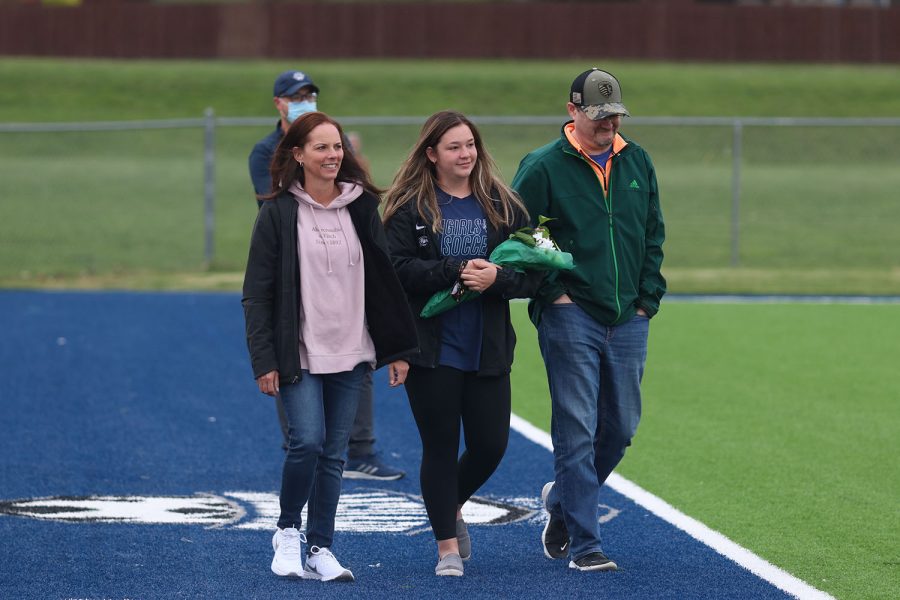 Walking with her parents, senior girls soccer manager Ryleigh Reigle holds a bouquet of flowers as she approaches the middle of the field. 