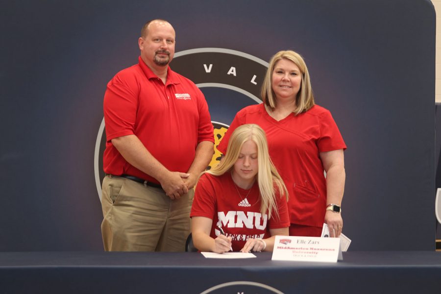 Senior Elle Zars signs and poses with her parents. Elle, the third Zars child and a 2021 graduate, currently attends MidAmerica Nazarene University and competes on their track and field.